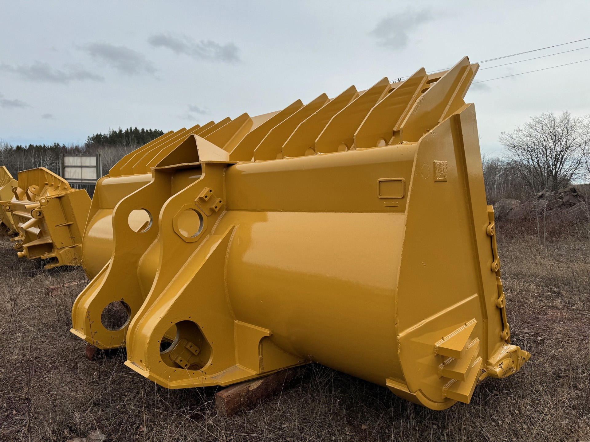 Large yellow industrial bucket attachments stacked in a yard, ready for use.