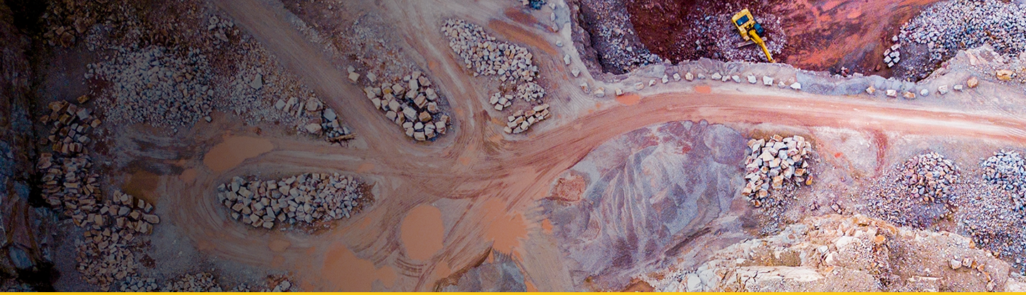 Aerial view of a quarry with winding dirt roads, rock piles, and a yellow construction vehicle.